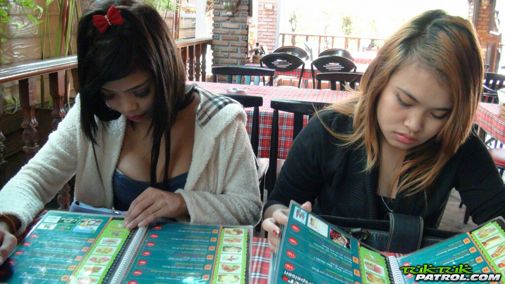 Two girls seated together in restaurant reading menus